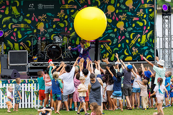 Kids crowded around a stage watching a magic performance featuring a large yellow balloon.