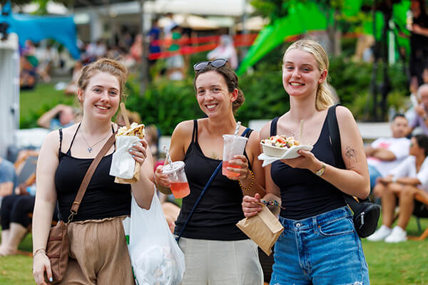 Three women holding various food and drinks smiling at the camera.