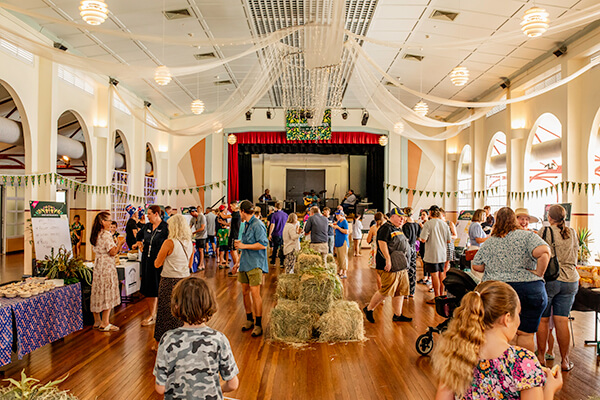 A crowd of people in a hall walking around market stalls.