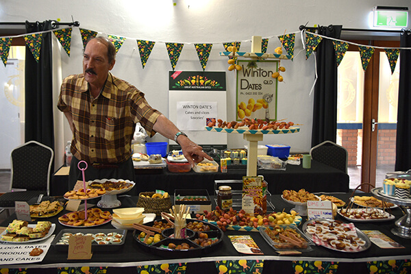 A man standing behind a table filled with platters of local food.